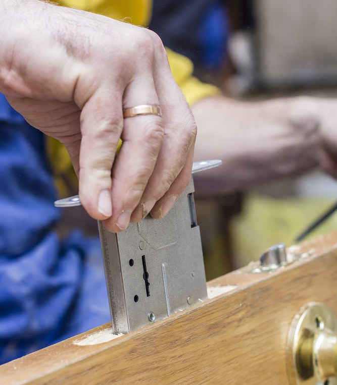 Installation Serrure à Mortaise sur Porte en Bois Installation d'une serrure à mortaise dans une porte en bois par un serrurier professionnel lors de travaux.