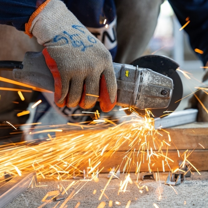 Meuleuse d'angle et découpe de métal : sécurité au travail Travailleur utilisant une meuleuse d'angle sur du métal avec des gerbes d'étincelles et gants de protection.